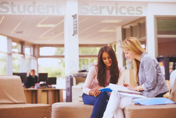 two females sitting chatting looking at a book